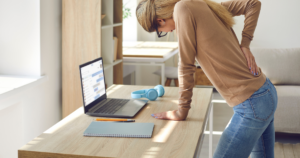 Woman standing and leaning on desk showing sciatica vs herniated disc with nerve compression causing leg pain